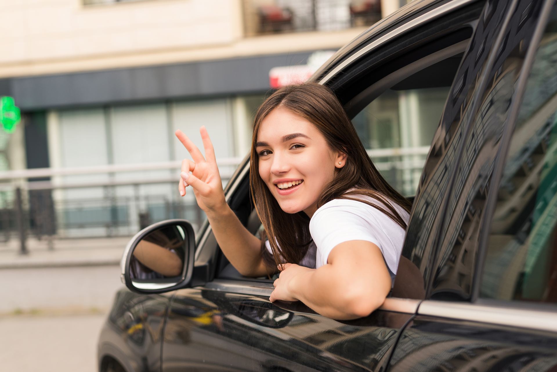 Conductora sonriente saludando desde la ventana de su auto